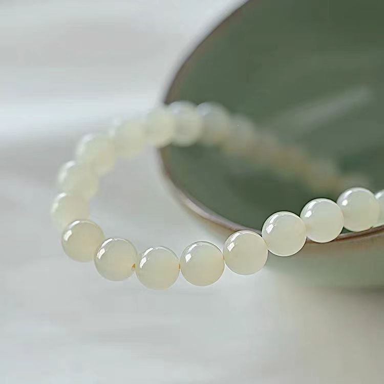 White beaded bracelet on a white surface with a blurred green object in the background
