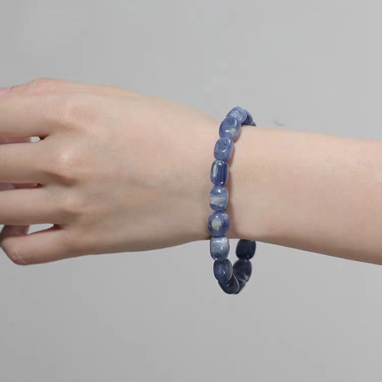 Hand wearing a blue beaded bracelet on a plain background