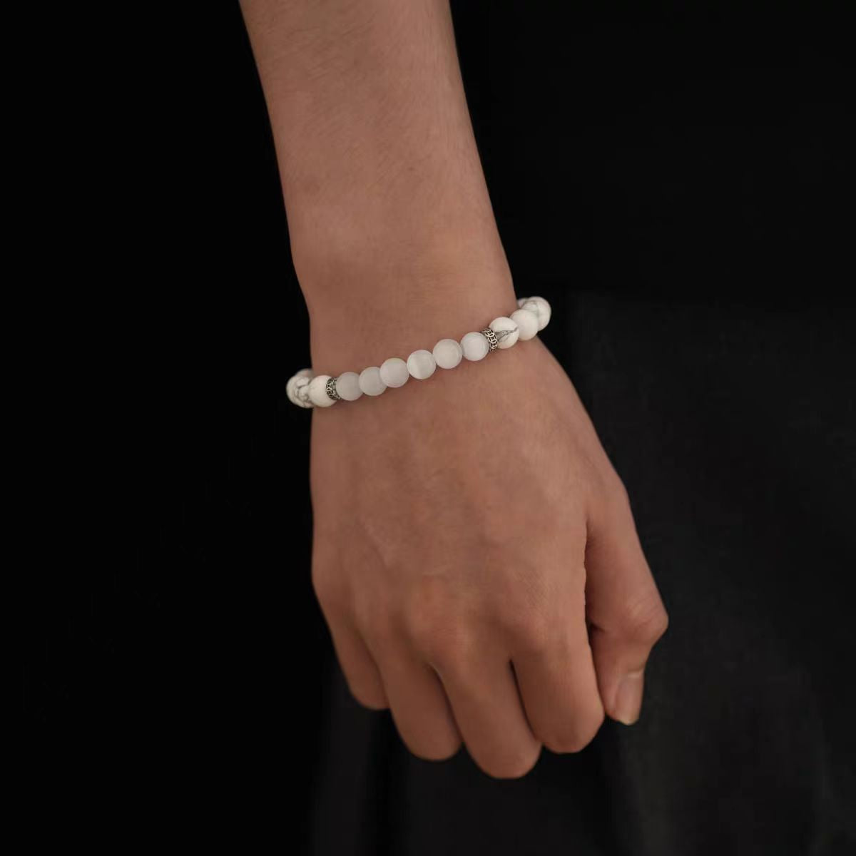 Hand wearing a beaded bracelet on a black background