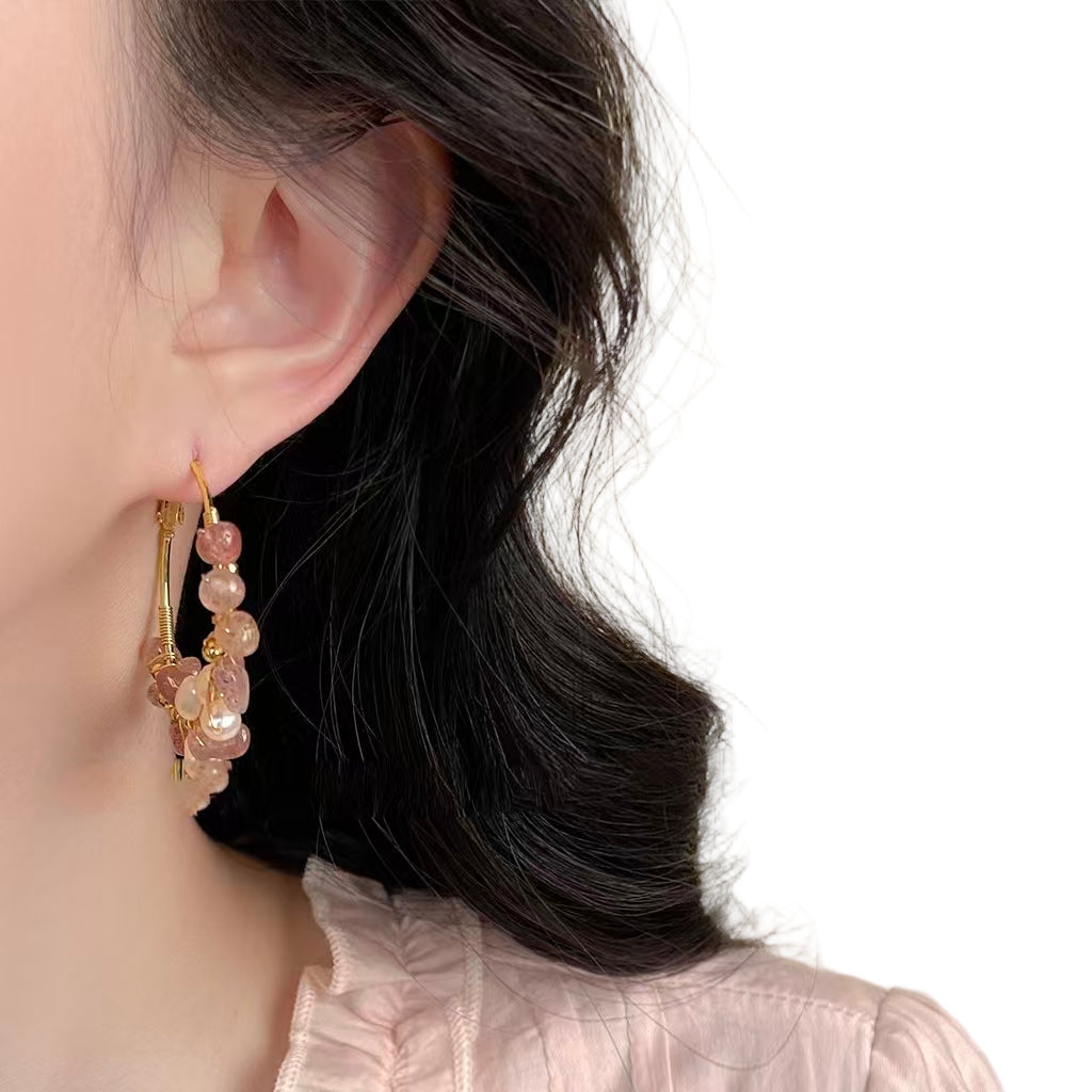Close-up of an ear wearing a gold hoop earring with pink gemstones on a white background.