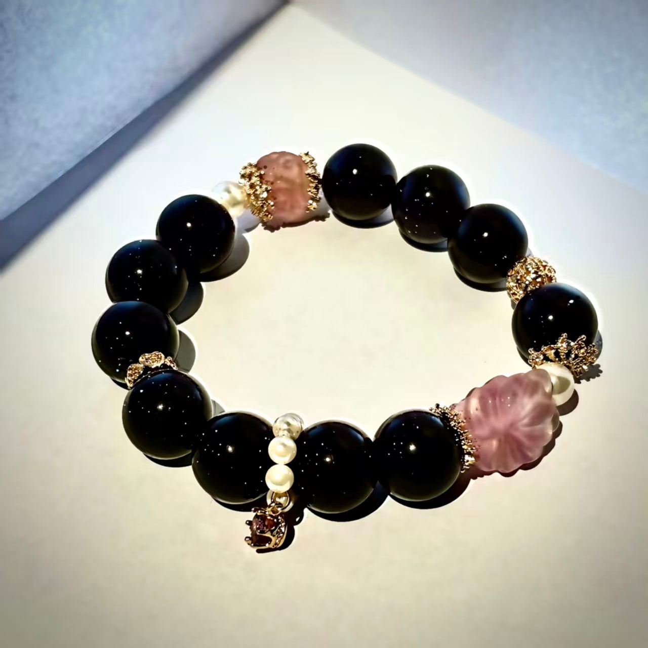 Black beaded bracelet with pink and gold accents on a light gray background