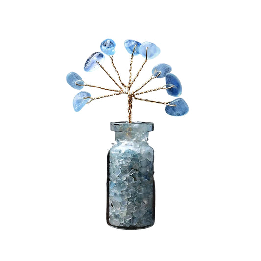 Decorative glass bottle with blue beads and a small tree on a dark background
