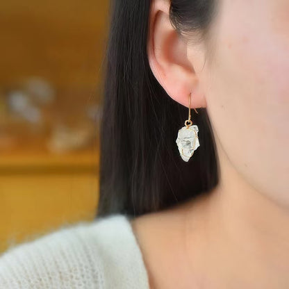 Close-up of a person wearing a gold earring with a clear gemstone against a blurred background.