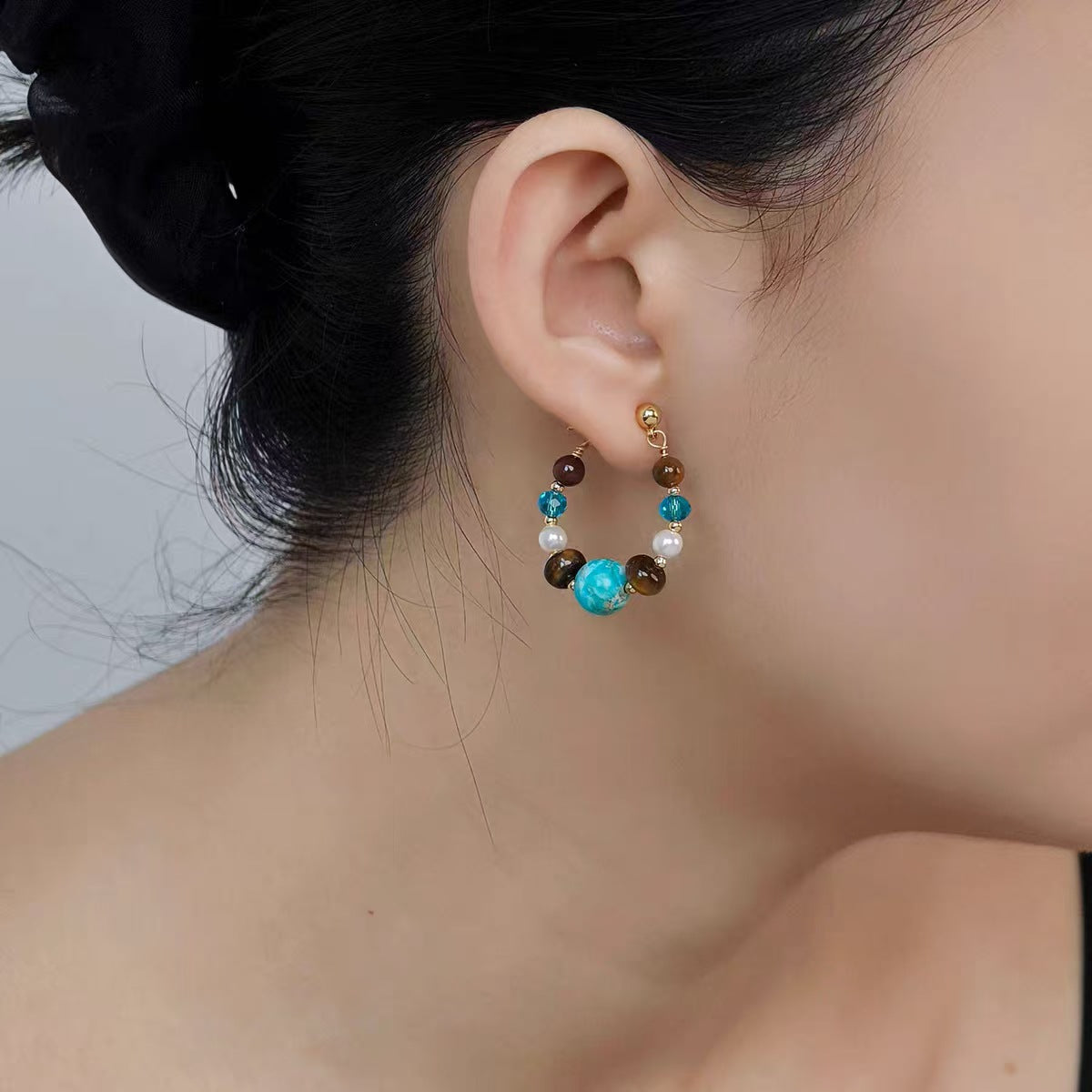 Close-up of an ear wearing a colorful beaded earring with a neutral background