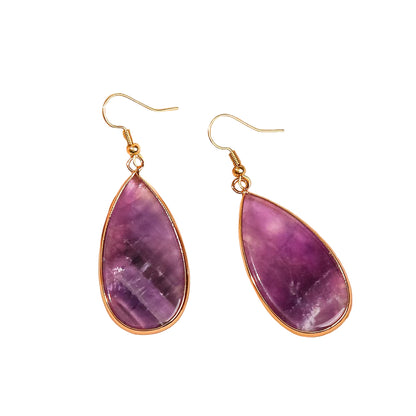Purple teardrop earrings with gold accents on a beige fabric background