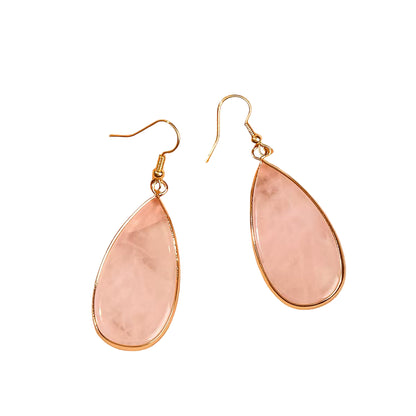 Teardrop-shaped pink earrings with gold accents on a soft pink fabric background