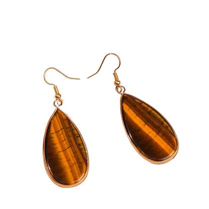 Teardrop-shaped tiger's eye earrings with gold hooks on a beige fabric background