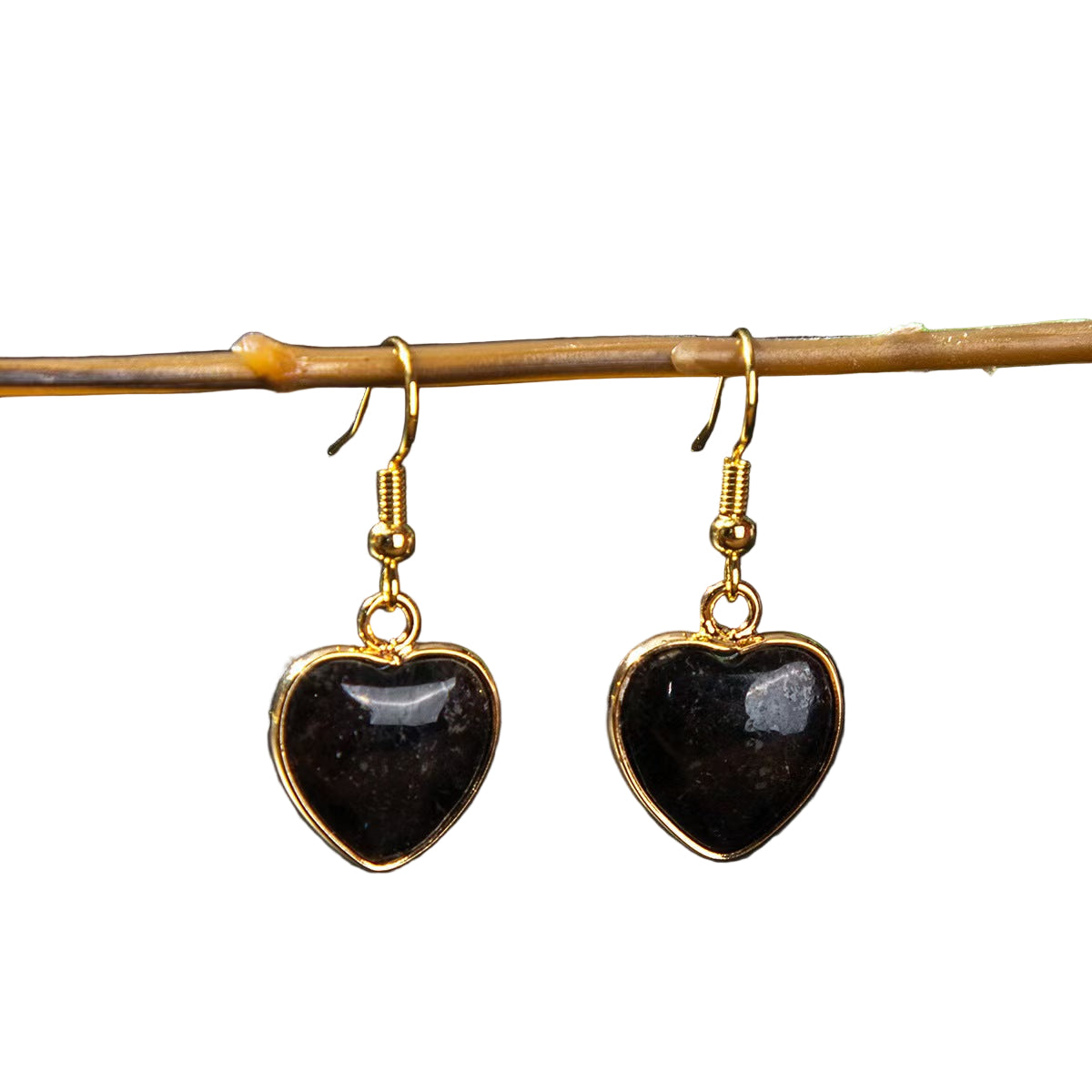 Heart-shaped black earrings with gold frames hanging on a branch against a dark background.