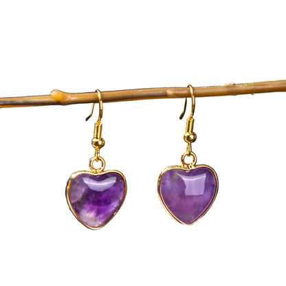 Heart-shaped purple earrings with gold accents on a dark background