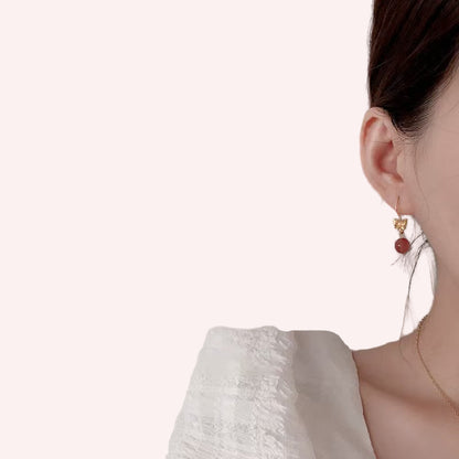 Close-up of a person wearing gold earrings with red stones against a neutral background