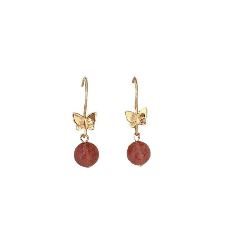 Gold butterfly earrings with red beads on a white surface