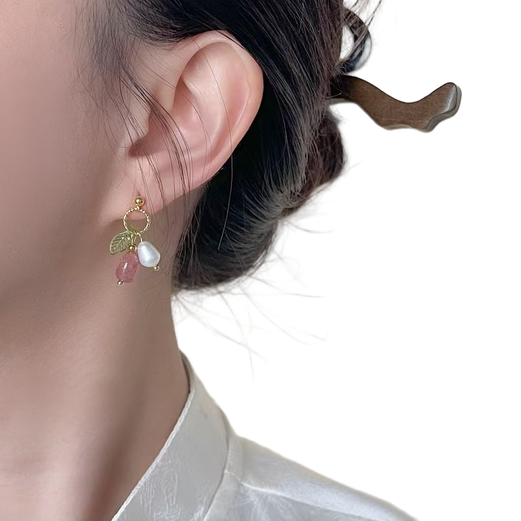 Close-up of an ear wearing a gold earring with a green leaf and white pearl design.