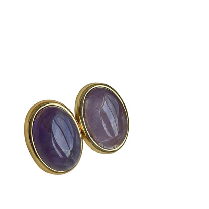 Gold earrings with purple stones in a jewelry box on a light blue background