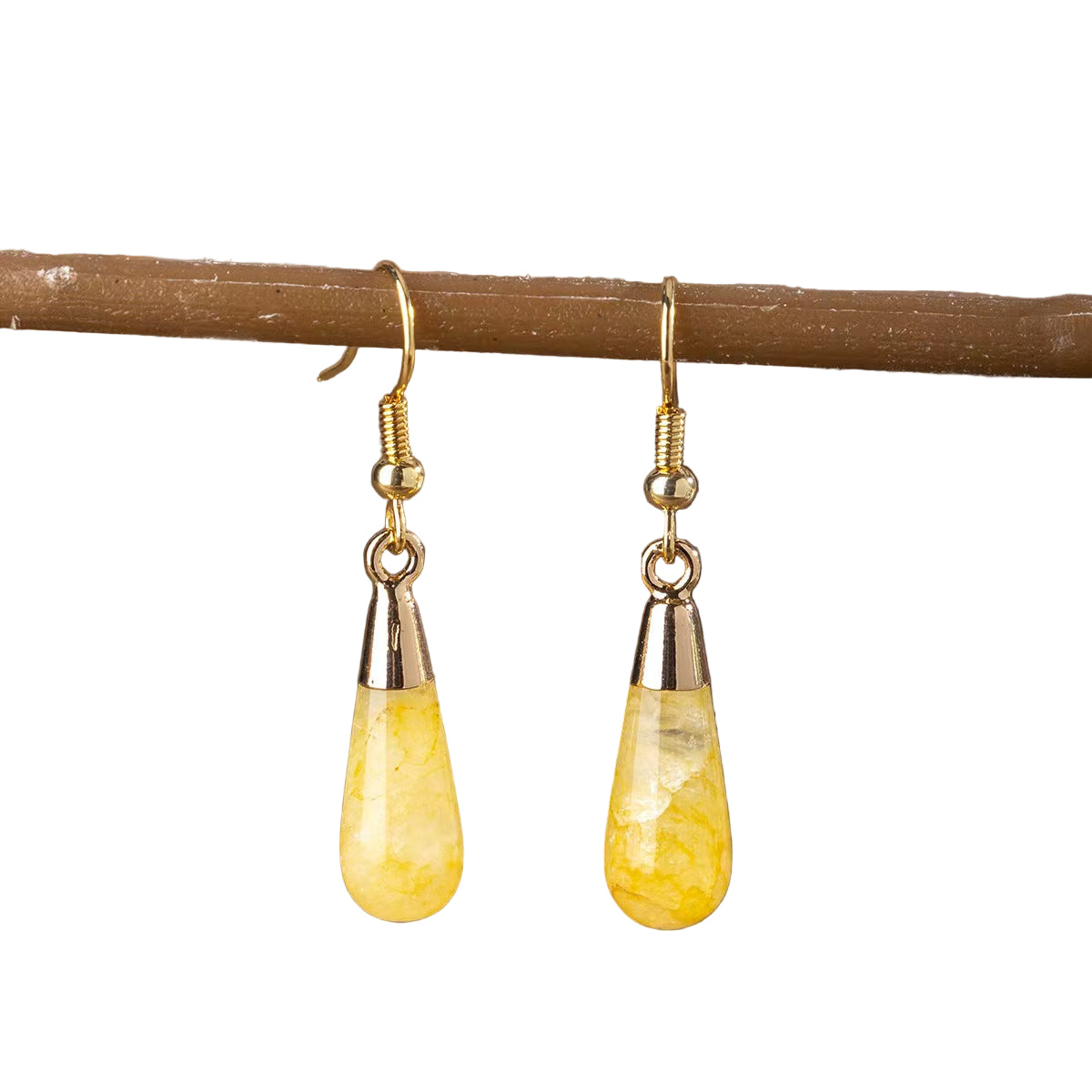 Yellow teardrop earrings with gold and silver accents on a wooden branch.