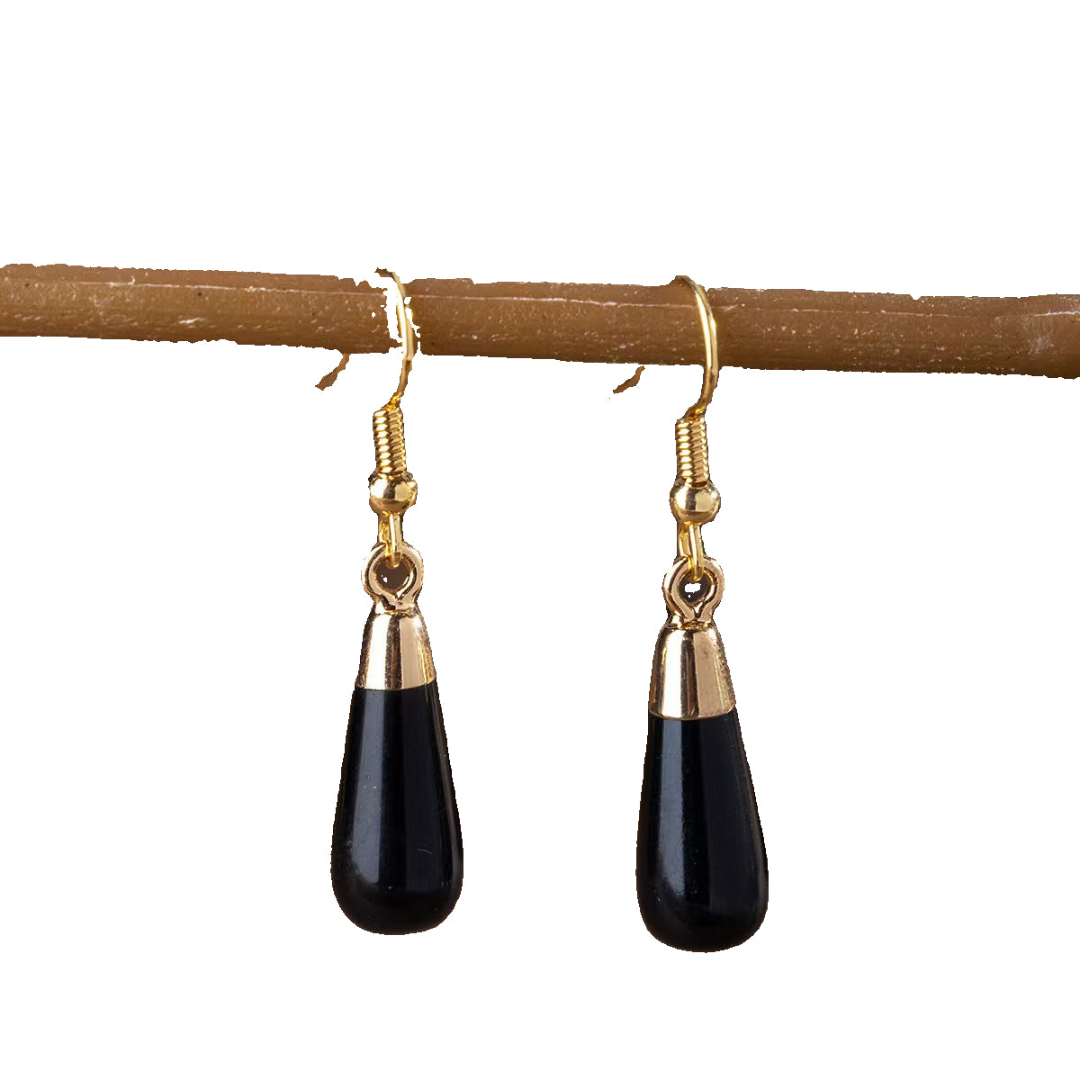 Black teardrop earrings with gold accents hanging on a branch.