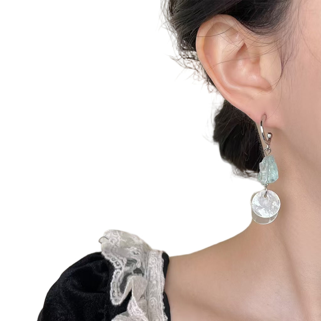 Close-up of a person wearing a silver earring with a clear stone on a white background