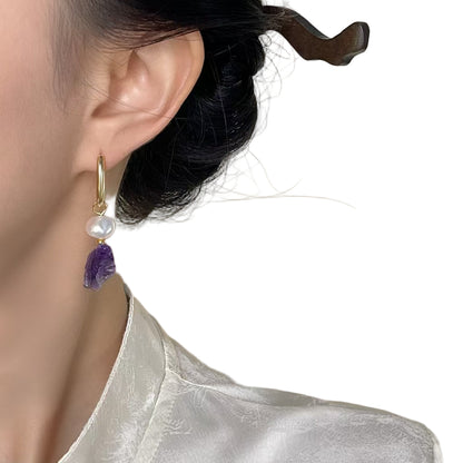 Close-up of an earring with a purple gemstone and pearl on a neutral background