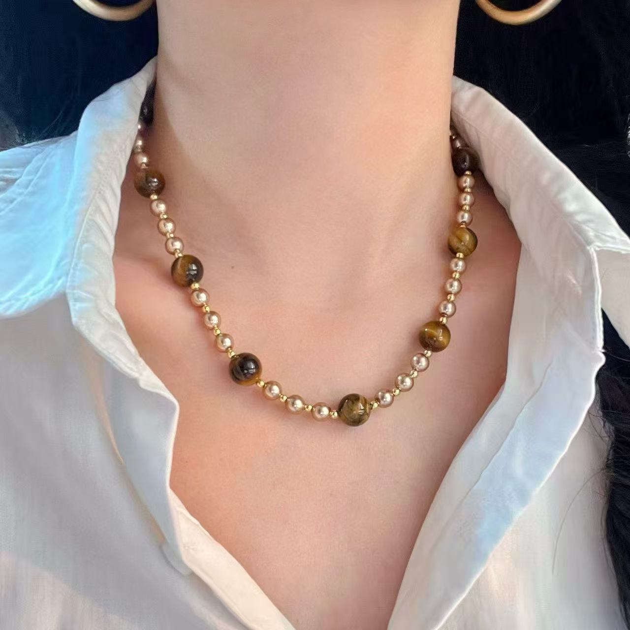 Necklace with brown and gold beads worn by a person in a white shirt.