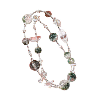 Hand holding a bracelet with green and clear beads on a light background