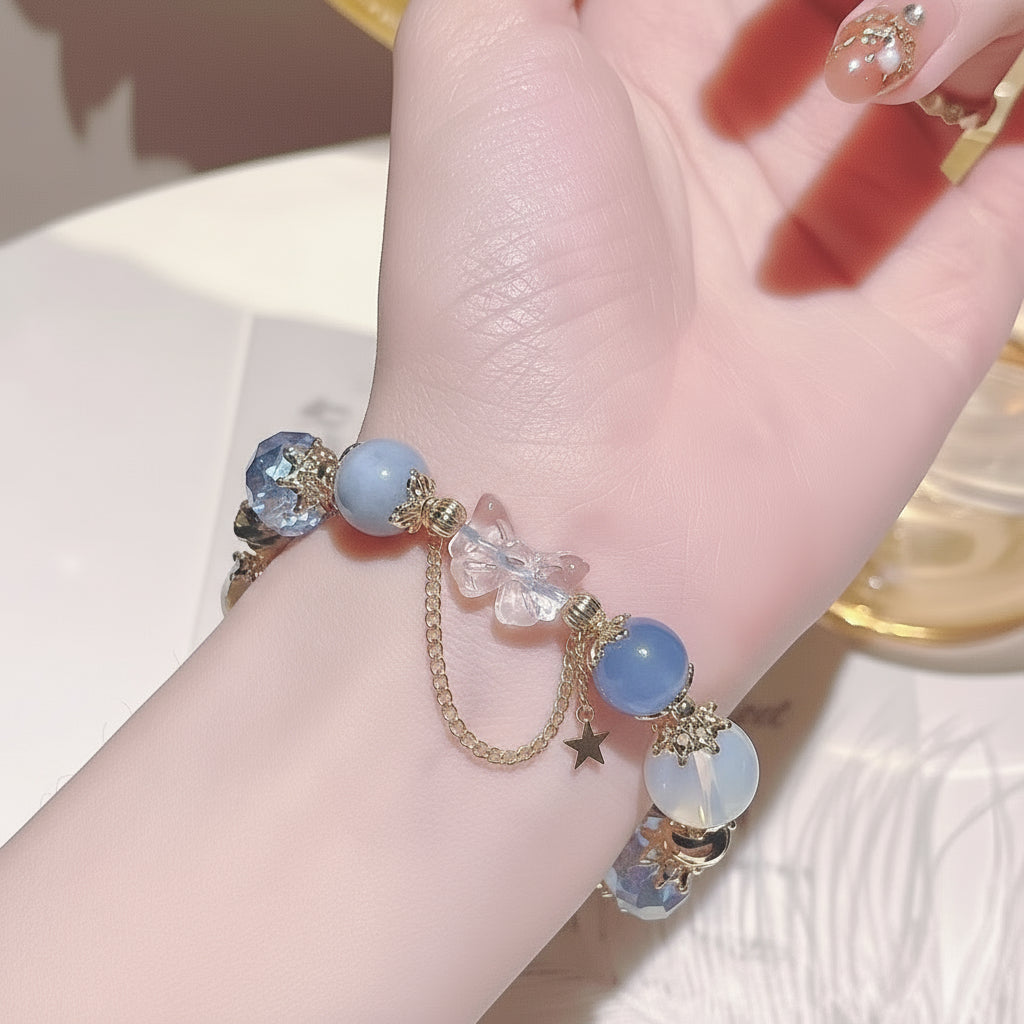 Hand wearing a bracelet with blue beads and gold accents on a light background