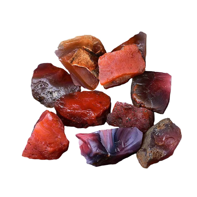 Collection of red and purple rough gemstones on a dark surface with a green plant.