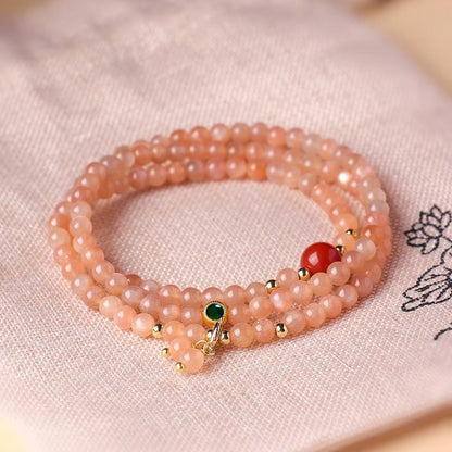 Pink beaded bracelet with green and red beads on a light pink fabric background