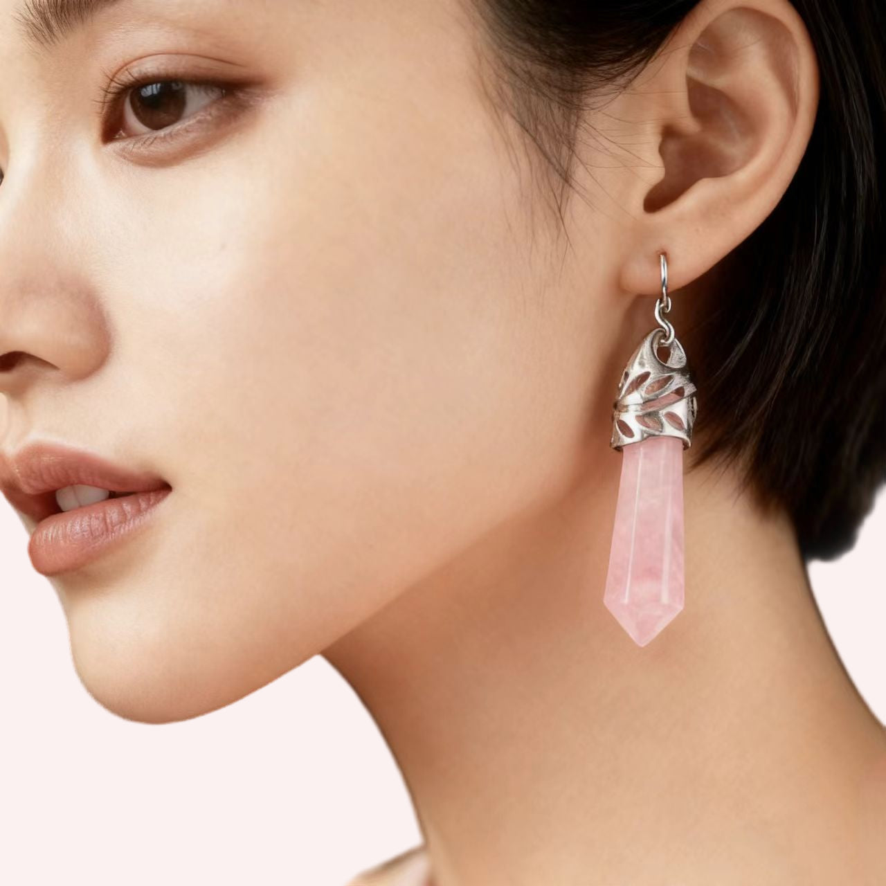 Close-up of a woman wearing a silver earring with a pink crystal pendant.