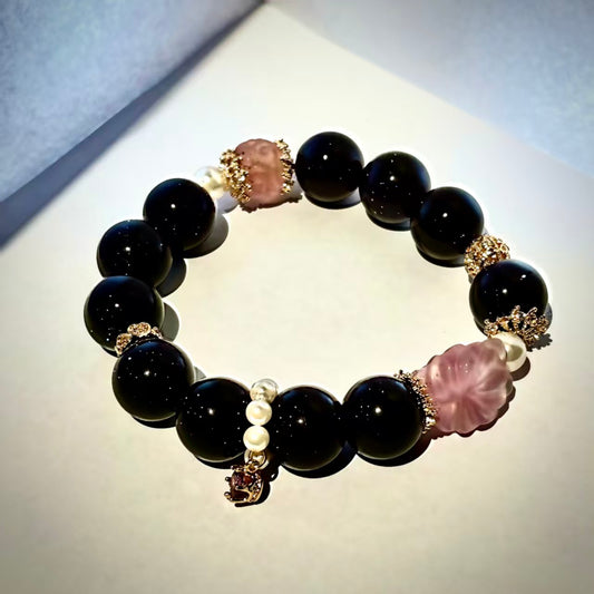 Black beaded bracelet with pink and gold accents on a light gray background