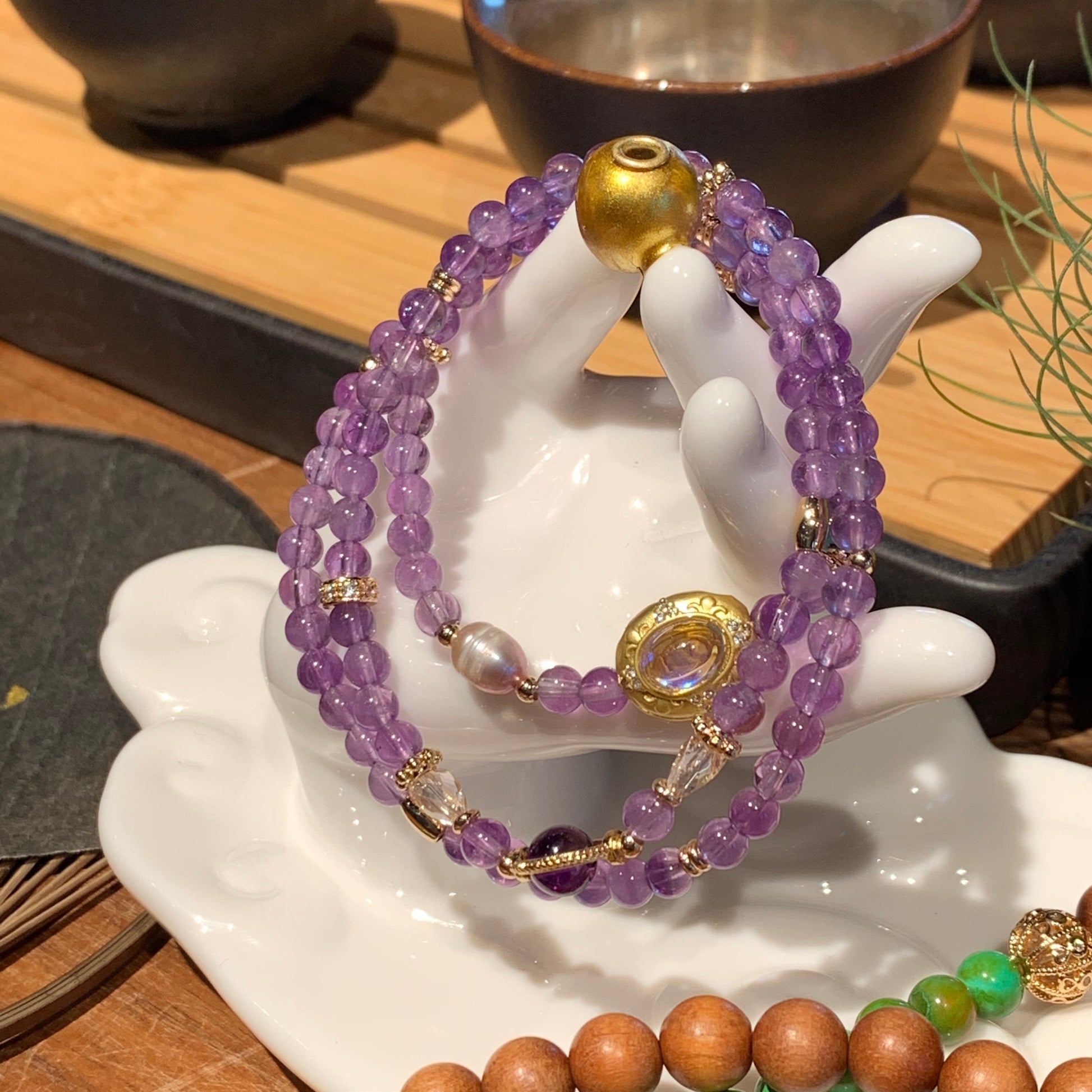 Amethyst beaded bracelet with gold accents on a white dish, with other bracelets in the background.