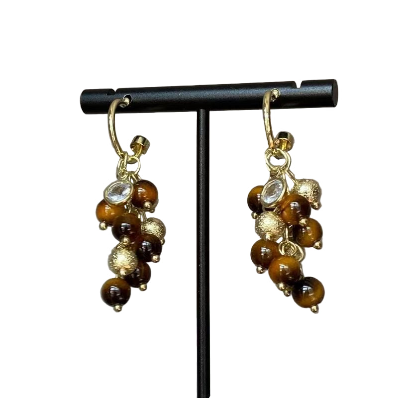Pair of gold and brown beaded earrings on a black stand against a gray background